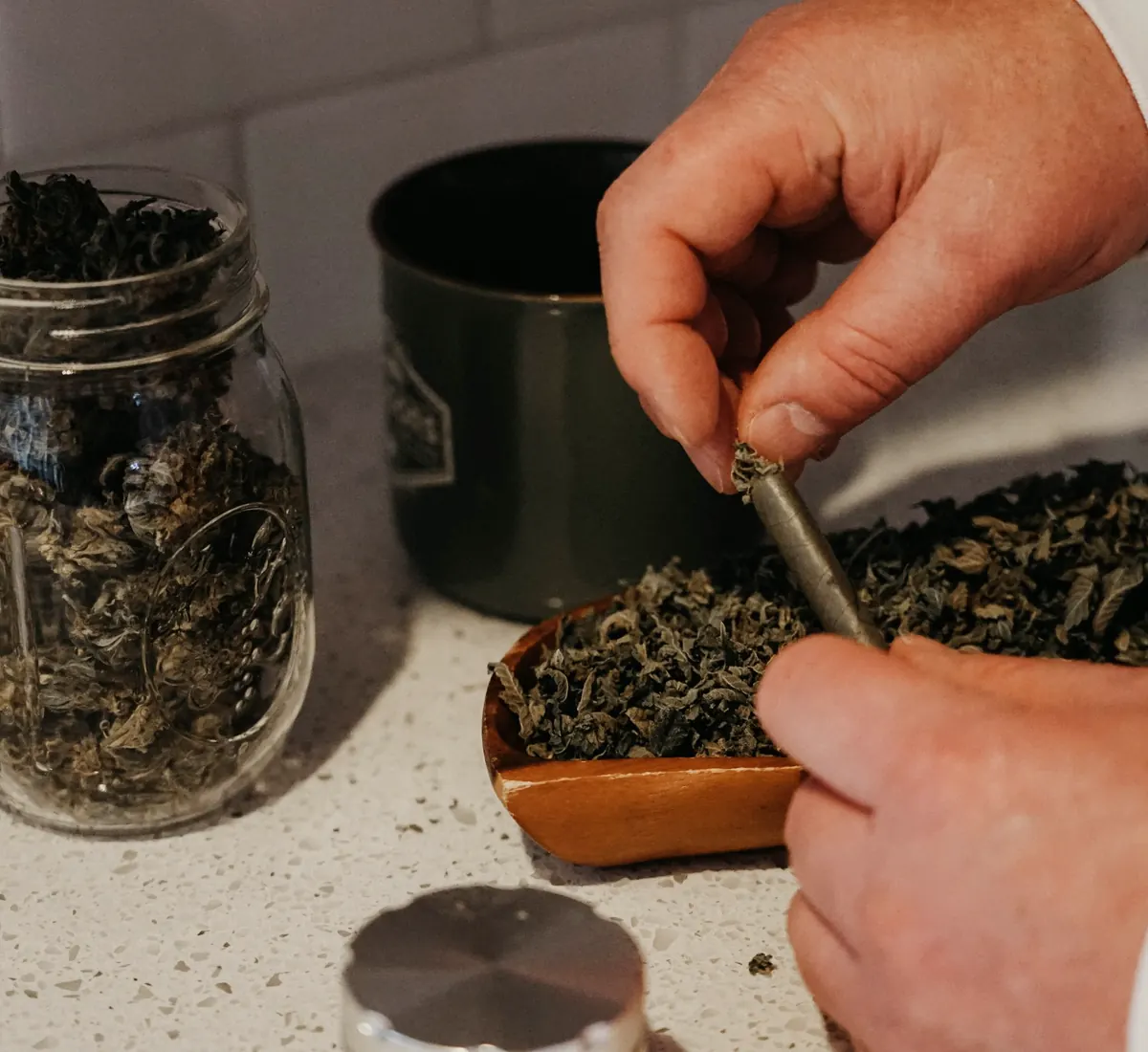 Hands packing cannabis from a tray into a glass jar